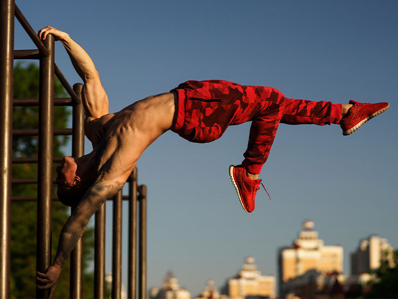 Hänge dich in die Ausgangsposition der Human Flag und ziehe dein oberes Bein angewinkelt zum Körper. Strecke dein unteres Bein nach oben durch.
