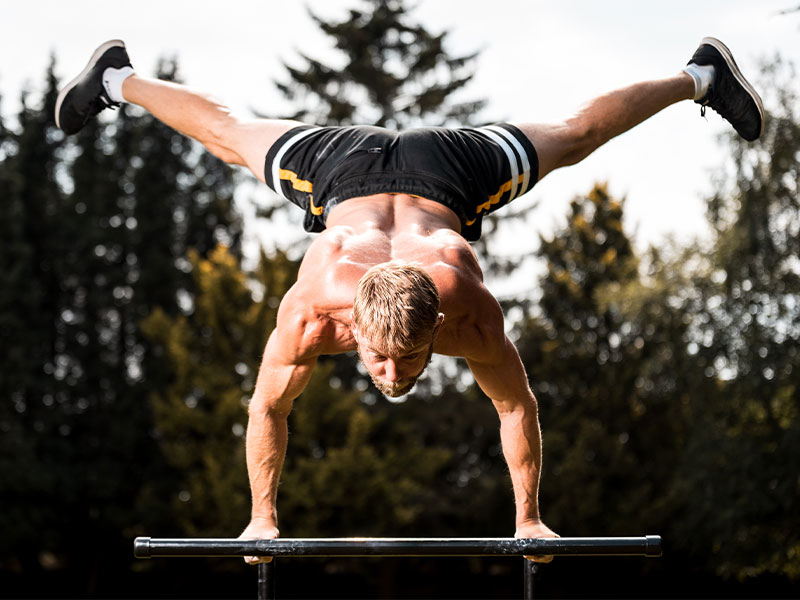 Hänge dich in die Ausgangsposition der Human Flag und spreize deine Beine weit voneinander ab. Dein Körper sieht optisch wie ein X aus.